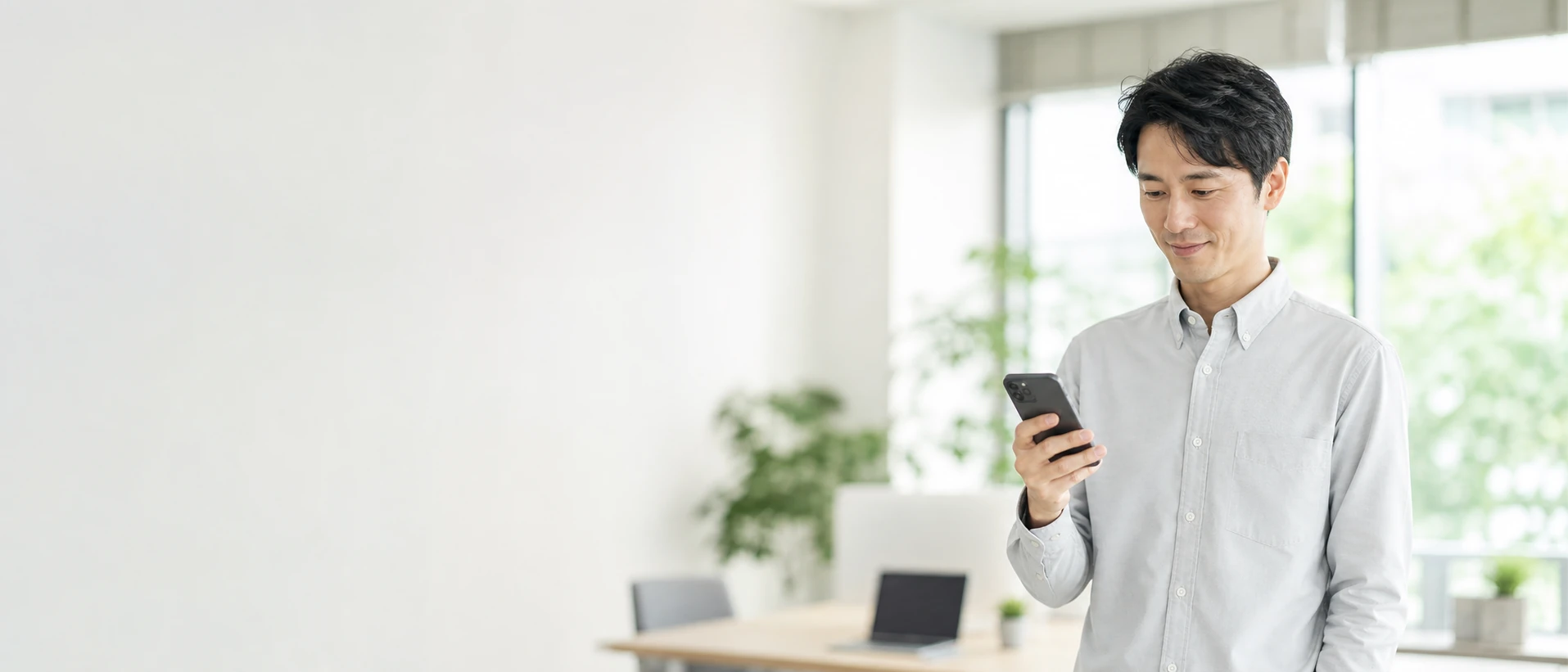 明るいオフィスでスマートフォンを見ている社員。LINEを入口に、スマホだけで業務が完結する様子。